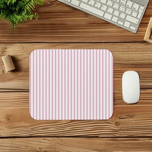 May include: A rectangular mouse pad with a vertical striped pattern in light pink and white. The mouse pad is on a wooden desk, with a white computer mouse and keyboard visible in the background.