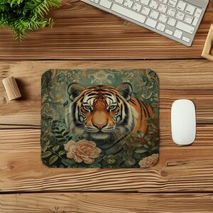 May include: Square mouse mat featuring a detailed illustration of a tiger's face. The tiger has orange and black stripes, with a pink nose and green eyes. The background is a floral design with roses.