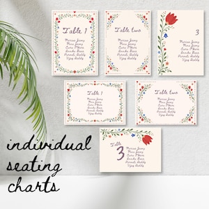May include: Individual seating charts with floral borders. The cards are cream-colored with text that reads "Table 1", "Table two", and "3". The names of guests are listed below the table numbers. The words "individual seating charts" are written in cursive.