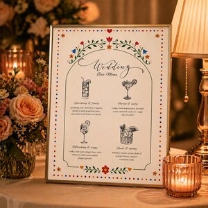 Whimsical floral wedding bar menu sign with colorful folk art border and illustrated drinks, editable Canva template displayed on easel and table settings