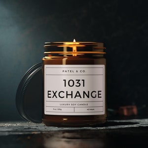 Könnte beinhalten: Eine brennende Sojakerze in einem braunen Glas mit goldenem Deckel. Das Etikett lautet "PATEL & CO. 1031 EXCHANGE LUXURY SOY CANDLE" mit einer Brenndauer von 40 Stunden. Das Glas ist 255g.