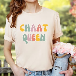 May include: A light beige t-shirt with the text "CHAAT QUEEN" in colourful, retro-style lettering.