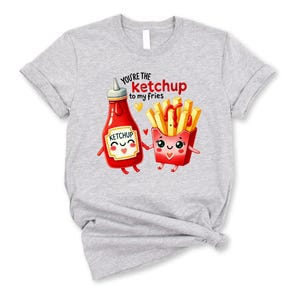 May include: Gray t-shirt with a cartoon ketchup bottle and french fries. The text on the shirt reads "You're the ketchup to my fries".