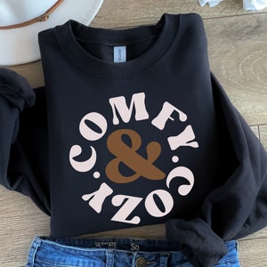 May include: Black sweatshirt with a pink and brown circle graphic that says "Comfy & Cozy" in a retro font.