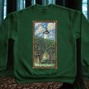 May include: A green sweatshirt with a framed image of a white tower with a green roof surrounded by trees. The tower is in a clearing in the woods. The image is surrounded by a gold frame with red and orange accents.