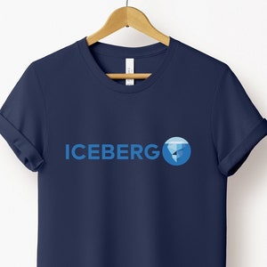 May include: Navy blue t-shirt with the word "ICEBERG" in blue, accompanied by a blue graphic of a globe and iceberg. The short-sleeved shirt is hanging on a wooden hanger against a white background.