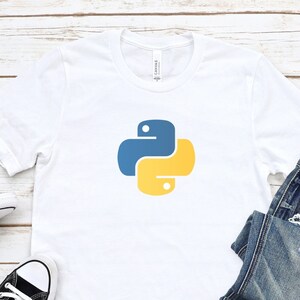 May include: White t-shirt with a blue and yellow Python logo. The t-shirt is laying on a wooden surface with a pair of black sneakers and blue jeans.