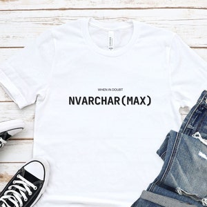 May include: White t-shirt with the text "WHEN IN DOUBT NVARCHAR(MAX)" printed on the front. The shirt is laid flat on a wooden surface with a pair of black Converse sneakers and a pair of blue jeans.