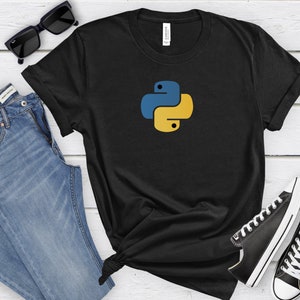 May include: Black t-shirt with a yellow and blue Python logo. The t-shirt is on a white wooden surface with a pair of blue jeans, sunglasses, and black sneakers.