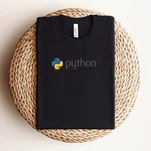 Peut inclure: T-shirt noir avec un logo Python jaune et bleu et le mot "python" en blanc.