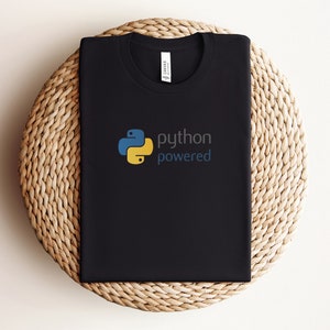 Peut inclure: T-shirt noir avec un logo Python jaune et bleu et le texte "python powered".