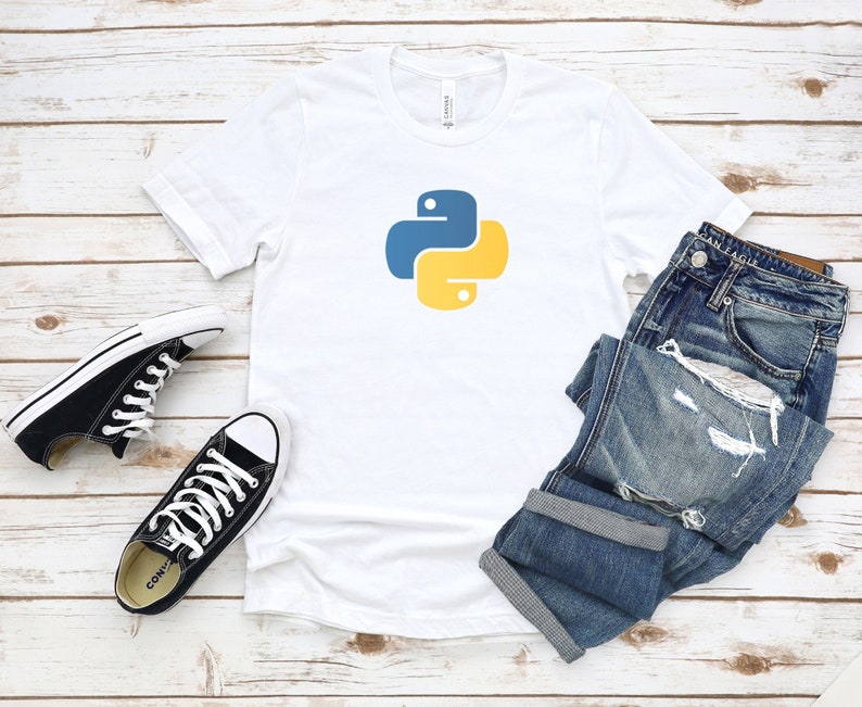 May include: White t-shirt with a blue and yellow Python logo. The t-shirt is laying on a wooden surface with a pair of black sneakers and blue jeans.