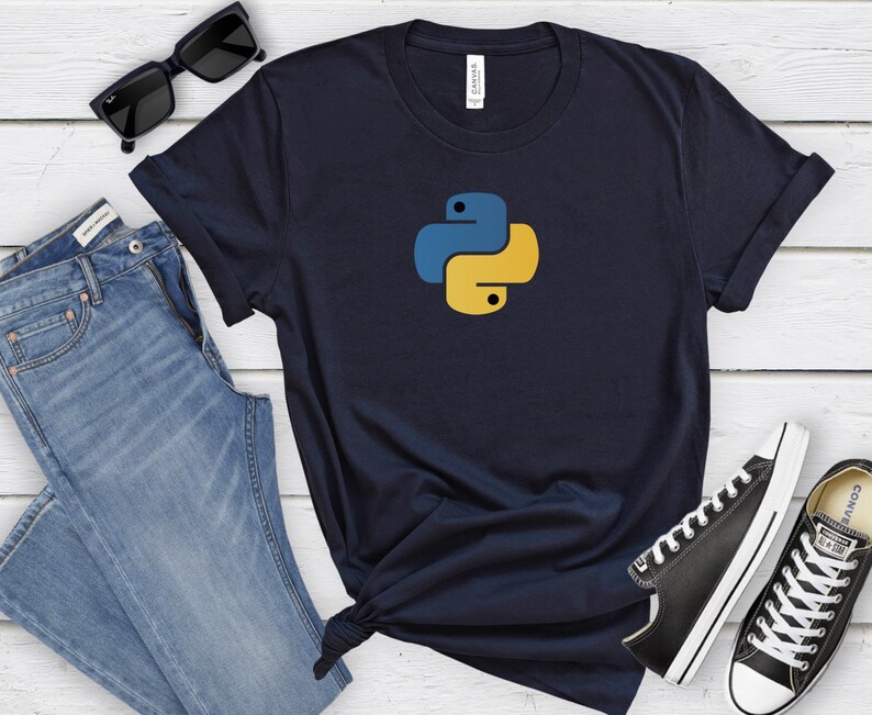 May include: A navy blue t-shirt with a yellow and blue Python logo. The t-shirt is on a white wooden surface with a pair of blue jeans, sunglasses, and black sneakers.
