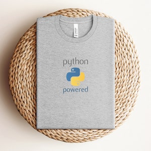 Pode incluir: Uma camiseta cinza com o texto "python powered" e um logotipo de python amarelo e azul.
