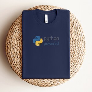 Peut inclure: Un t-shirt bleu marine avec un logo Python jaune et bleu et le texte "python powered".