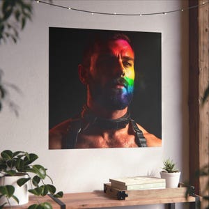 Peut inclure: Impression carrée représentant un homme avec le visage et la barbe peints aux couleurs de l'arc-en-ciel. Il porte un collier et un harnais en cuir noir. Le fond est sombre.