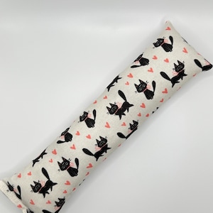 May include: A long, rectangular catnip toy with a white fabric cover. The fabric has a repeating pattern of black cats with pink bows and pink hearts.