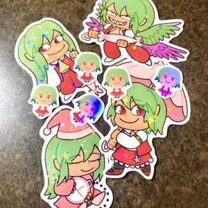 Può includere: Una collezione di adesivi olografici con personaggi dei cartoni animati con capelli verdi e occhi rossi. Gli adesivi raffigurano varie pose e abiti, tra cui un cappello da Babbo Natale e ali. Gli adesivi hanno una finitura scintillante e iridescente.