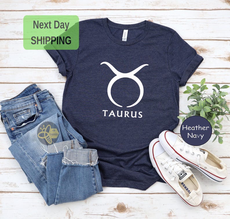 May include: A navy blue t-shirt with a white Taurus zodiac symbol and the word "Taurus" printed on the front. The shirt is made of a soft, comfortable material and is perfect for everyday wear.