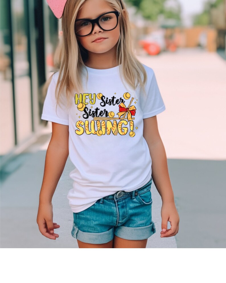 May include: White t-shirt with a graphic of a baseball bat and baseballs with the text "Hey Sister Sister Swing!"