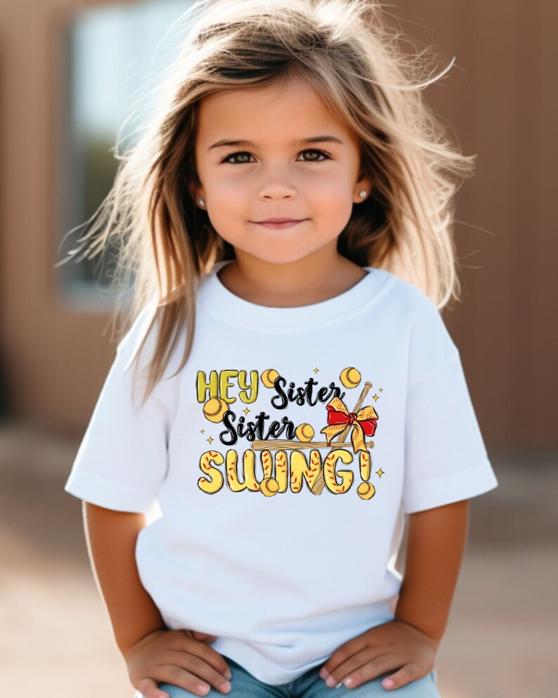 May include: White t-shirt with a yellow and black graphic that says "Hey Sister Sister Swing!" with a baseball bat, baseballs, and a red bow.