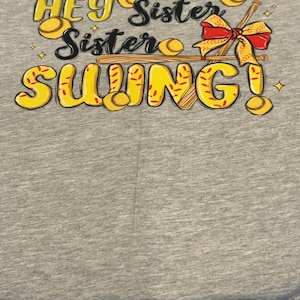 May include: Gray t-shirt with a yellow and red graphic design that says "Hey Sister Sister Swing!" with baseball bats and baseballs.