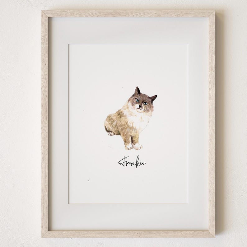May include: A framed watercolour print featuring a cat named Frankie. The cat is rendered in brown, beige, and grey tones, with a white chest and paws. The cat is seated and facing forward. The name "Frankie" is written in cursive script beneath the cat.