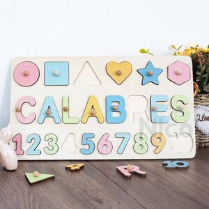 May include: Wooden puzzle board with colorful shapes, letters spelling "CALABRES", and numbers 1 through 10. The puzzle pieces are missing from the board and are scattered on a wooden surface.