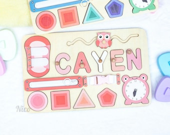 Könnte beinhalten: Holz-Lernspielzeug mit dem Namen "CAYEN" in rosa Buchstaben. Das Spielzeug enthält Formen, eine Uhr, eine Schnalle und einen Schieber. Das Design zeigt eine Eule und den Namen "Nico".