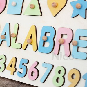 May include: A wooden board with colorful shapes and letters. The shapes include a circle, square, triangle, heart, and star. The letters spell out the name "ALABRE". The board also has numbers 3 through 9.