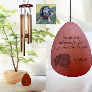 May include: A wooden wind chime with a brown, teardrop-shaped charm. The charm has a black and white photo of a dog and the text "Hear the wind and think of me for in your heart I'll always be Lucas 2016-2024".
