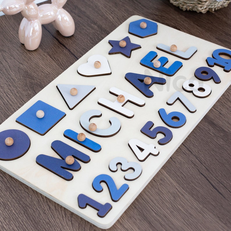 May include: Wooden puzzle board with blue and white painted shapes and letters spelling out the name "MICHAEL" and numbers 1 through 9. The puzzle pieces are removable and have small wooden knobs for easy handling.