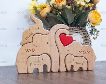 Peut inclure: Puzzle en bois en forme de famille d'éléphants avec un cœur rouge au centre. Les éléphants sont étiquetés "Papa", "Maman", "Daniel", "Sammy" et "Tomy".