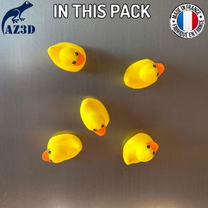 Puede incluir: Cinco peque&ntilde;os imanes de pato de goma amarillos con picos naranjas y ojos negros. El texto IN THIS PACK est&aacute; centrado en la parte superior, con un logotipo de AZ3D a la izquierda y un logotipo circular de MADE IN FRANCE a la derecha.