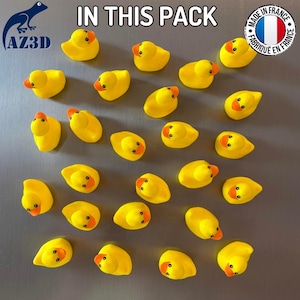 Puede incluir: Una colecci&oacute;n de veintid&oacute;s patitos de goma amarillos dispuestos en un patr&oacute;n de cuadr&iacute;cula. Cada pato presenta un pico naranja brillante y ojos negros. El texto IN THIS PACK aparece en la parte superior, junto a un logo AZ3D y un emblema circular de la bandera francesa.