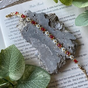 May include: A red and white beaded bracelet with gold accents. The bracelet is lying on a book with the text "Night Road" visible.