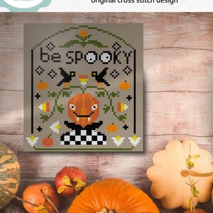 Könnte beinhalten: Ein digitales Kreuzstichmuster mit einem grinsenden Kürbis und dem Text "be SPOOKY". Das Muster ist umgeben von schwarzen Vögeln, Zuckermais und anderen Halloween-Motiven.