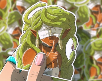 May include: A sticker featuring a woman with green snakes for hair, wearing a blindfold and a choker. She is holding her finger to her lips, as if to tell someone to be quiet. The sticker has a white border.