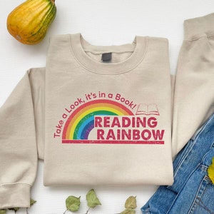 May include: A beige sweatshirt with a rainbow and the text "Take a Look, it's in a Book! Reading Rainbow" printed on the front.