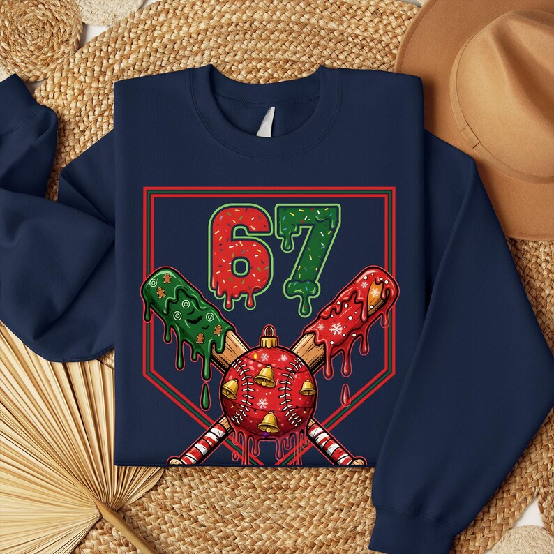 May include: Navy blue sweatshirt with a baseball-themed Christmas design. The graphic features the number 67 in red and green, crossed baseball bats, and a baseball with bells and snowflakes. The design is set within a red and green baseball diamond.