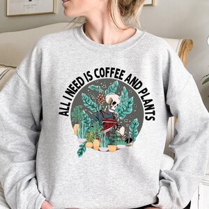 May include: Gray sweatshirt with a graphic of a skeleton holding a coffee cup and watering plants. The text reads "All I need is coffee and plants."