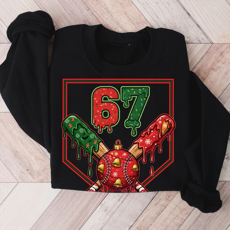 May include: Black sweatshirt featuring a baseball-themed design. The graphic includes the number "67" in red and green, crossed baseball bats, and a red baseball ornament with gold bells. The design has a festive, holiday theme.