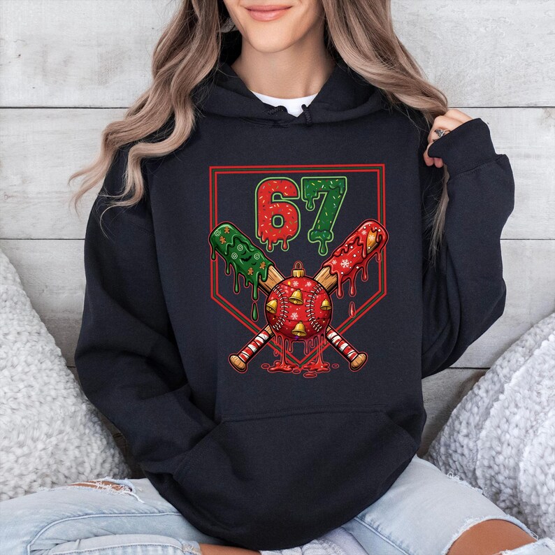 May include: Black hoodie featuring a baseball-themed Christmas design. The graphic includes crossed bats, a baseball ornament, and the number "67" in red and green. The design has a festive, holiday theme.