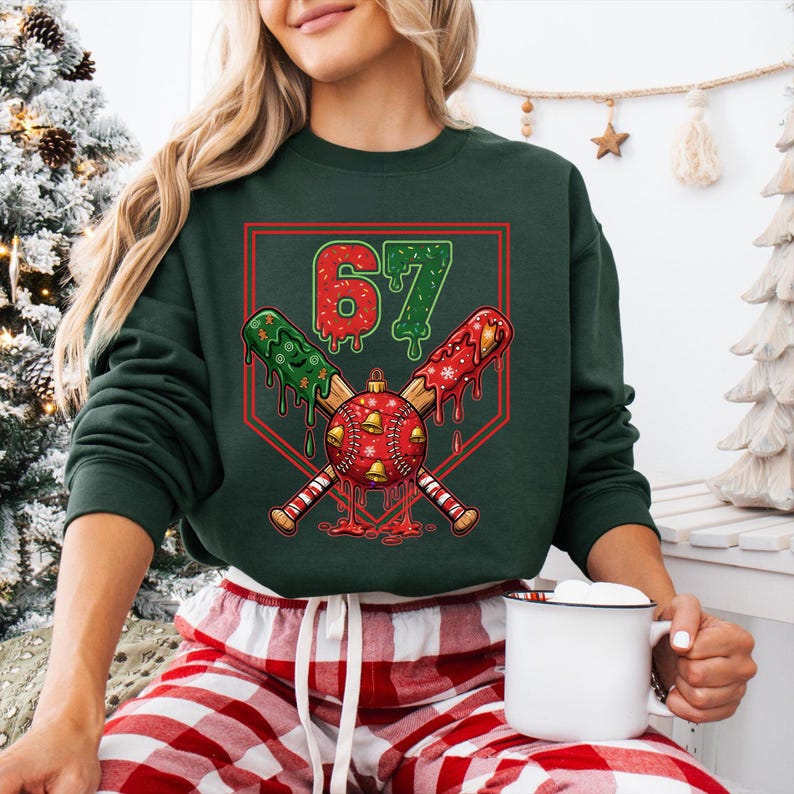 May include: Dark green sweatshirt with a baseball-themed Christmas graphic. The graphic features crossed baseball bats, a baseball ornament, and the number 67. The bats are decorated with red and green accents, and the ornament has gold bells.