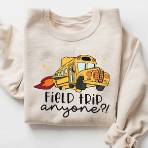 May include: A beige sweatshirt with a yellow school bus with a rocket booster and the text "Field Trip anyone?!"