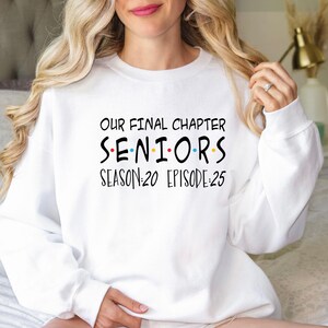 May include: White sweatshirt with the text "Our Final Chapter Seniors Season:20 Episode:25" in black. The word "Seniors" has colorful dots between the letters.