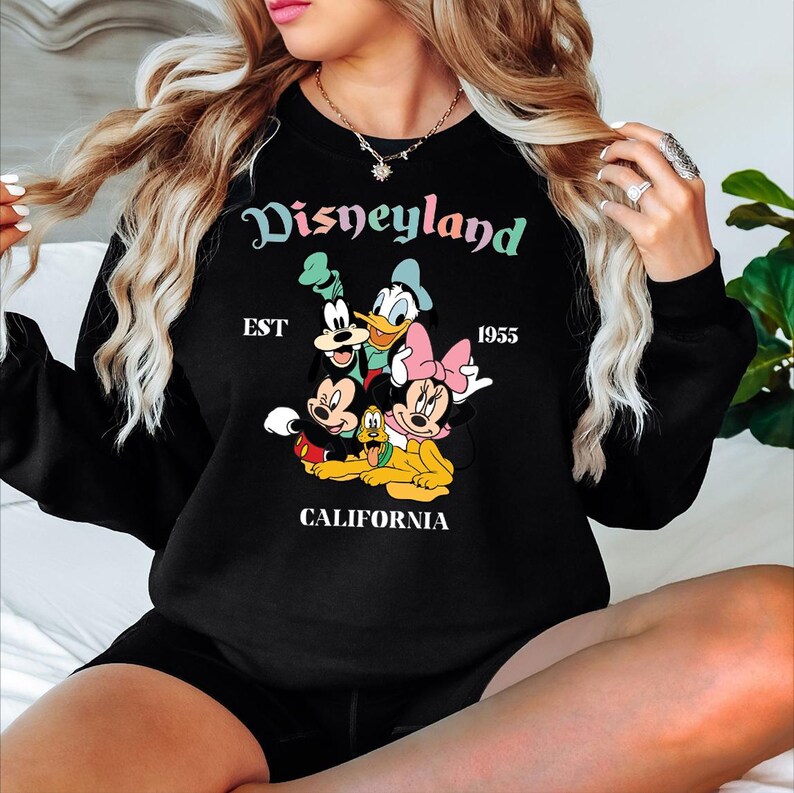 Puede incluir: Sudadera negra con el logotipo de Disneyland y los personajes de dibujos animados Mickey Mouse, Minnie Mouse, Donald Duck, Goofy y Pluto. Tambi&eacute;n se muestra el texto "EST 1955 CALIFORNIA". La sudadera tiene cuello redondo y mangas largas.
