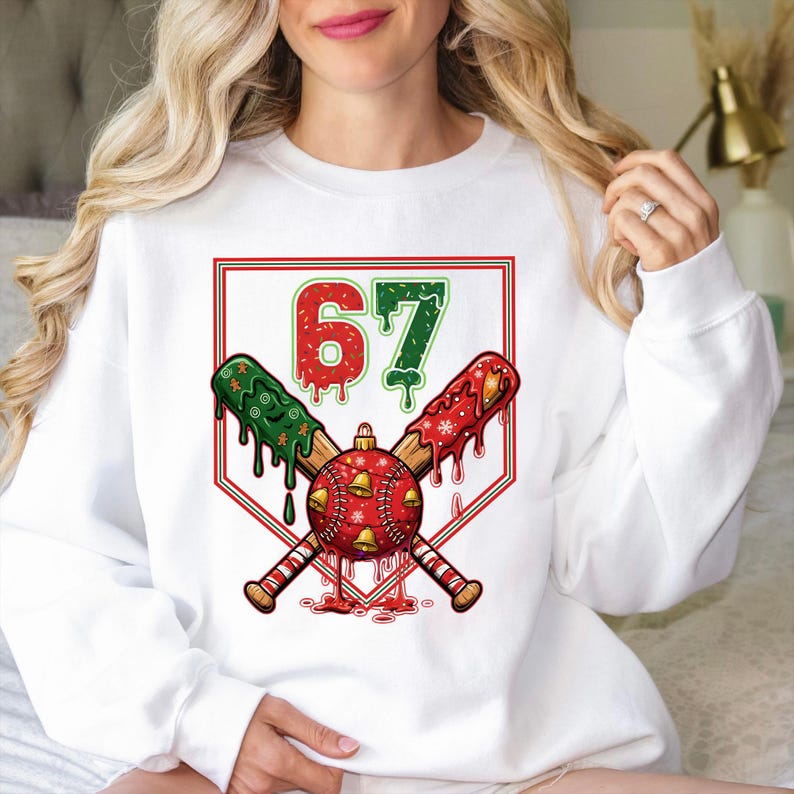 May include: White sweatshirt featuring a baseball-themed Christmas design. The graphic includes crossed baseball bats, a red ornament with bells, and the number 67 in red and green. The bats have green and red accents.