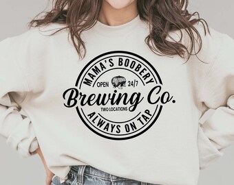 May include: A white sweatshirt with a black circle logo that says "Mama's Boobery Brewing Co. Open 24/7 Two Locations Always On Tap".