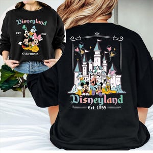 Puede incluir: Sudadera negra con dise&ntilde;o de Disneyland. La parte delantera muestra a Mickey, Minnie, Donald y Daisy Duck con "Disneyland Est. 1955 California." La parte trasera presenta un castillo y personajes con "Disneyland Est. 1955."